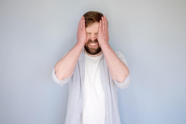 Hombre caucásico estresado o con dolor de cabeza, cerró los ojos, sostiene la cabeza y muestra los dientes