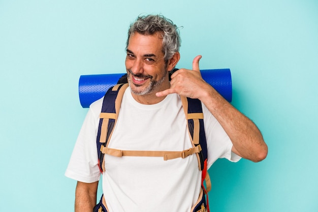 Hombre caucásico de excursionista de mediana edad aislado sobre fondo azul que muestra un gesto de llamada de teléfono móvil con los dedos.