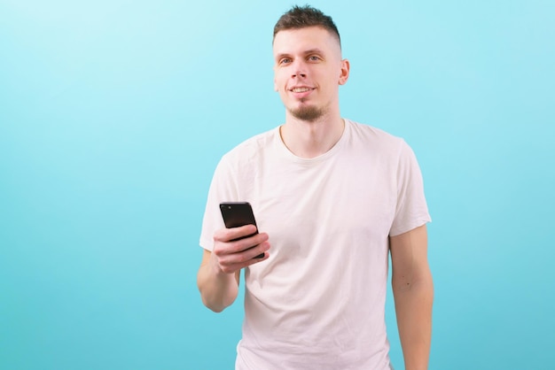 Hombre caucásico feliz sosteniendo su teléfono móvil negro y mirando a la cámara en un azul de moda