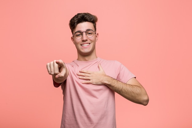 El hombre caucásico fresco joven apunta con el dedo pulgar lejos, riendo y despreocupado.