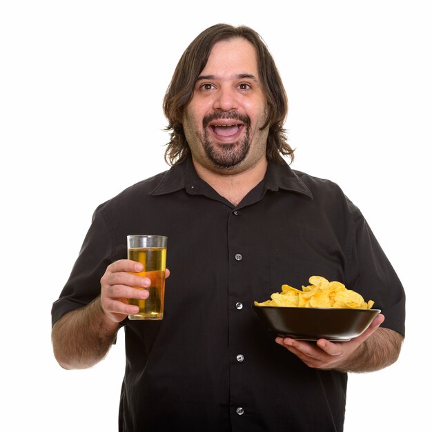 Hombre caucásico gordo feliz sonriendo mientras sostiene el tazón de patatas fritas y un vaso de cerveza