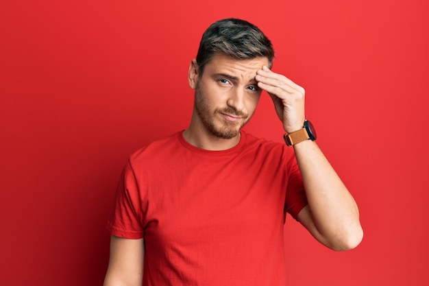 Hombre caucásico guapo con camiseta roja casual preocupado y estresado por un problema con la mano en la frente, nervioso y ansioso por la crisis