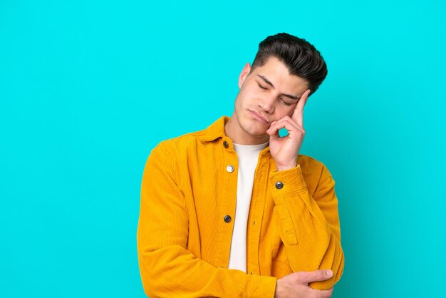 Hombre caucásico guapo joven aislado en bakcground azul con dolor de cabeza