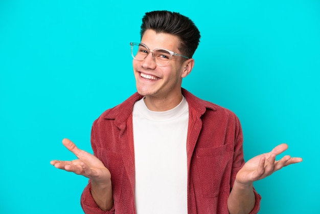 Hombre caucásico guapo joven aislado en bakcground azul con gafas y dudas