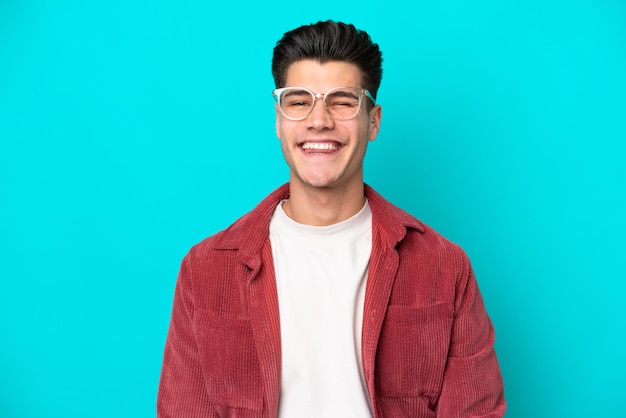 Hombre caucásico guapo joven aislado en bakcground azul con gafas y expresión feliz