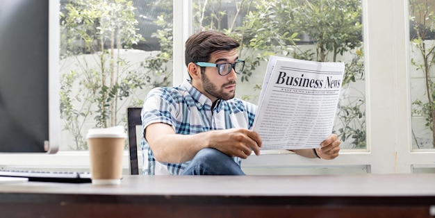 Hombre caucásico guapo leyendo noticias de negocios con sorpresa en casa por la mañana.