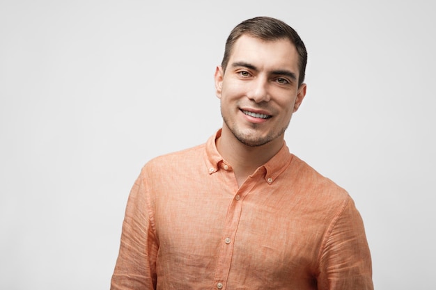 Hombre caucásico guapo sonriente de unos 30 años con camisa naranja en un retrato masculino de fondo gris