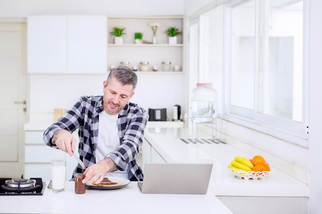 Hombre caucásico haciendo desayuno mientras trabaja