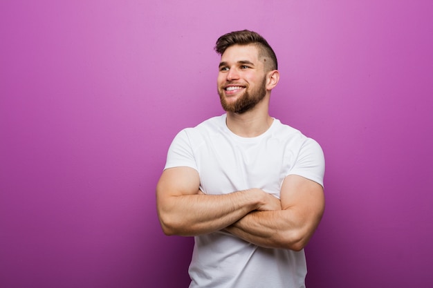 Hombre caucásico hermoso joven que sonríe confiado con los brazos cruzados.