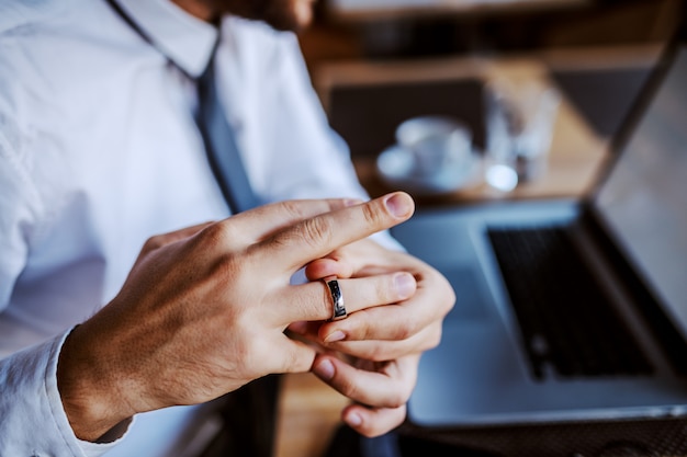 Hombre caucásico infiel en camisa y corbata quitándose el anillo de bodas. Enfoque selectivo en la mano.