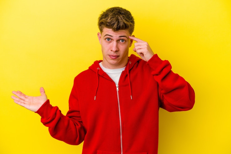 Foto hombre caucásico joven aislado en amarillo sosteniendo y mostrando un producto en la mano.