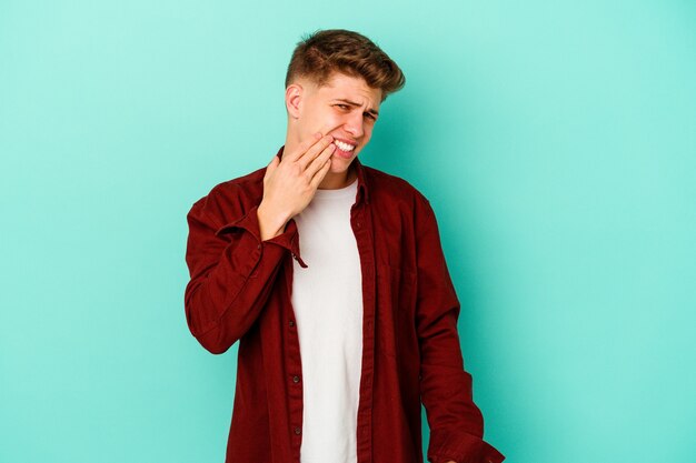 Hombre caucásico joven aislado en azul que tiene un fuerte dolor de dientes, dolor de muelas.