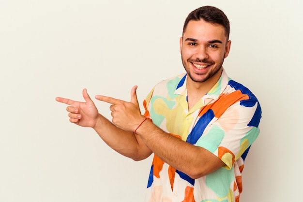 Hombre caucásico joven aislado en blanco apuntando con los dedos índices a un espacio de copia, expresando entusiasmo y deseo.