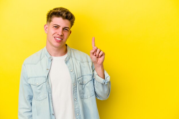 Hombre caucásico joven aislado en la pared amarilla que muestra el número uno con el dedo.