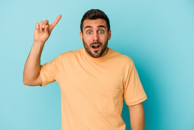 Hombre caucásico joven aislado en la pared azul con una gran idea, concepto de creatividad.