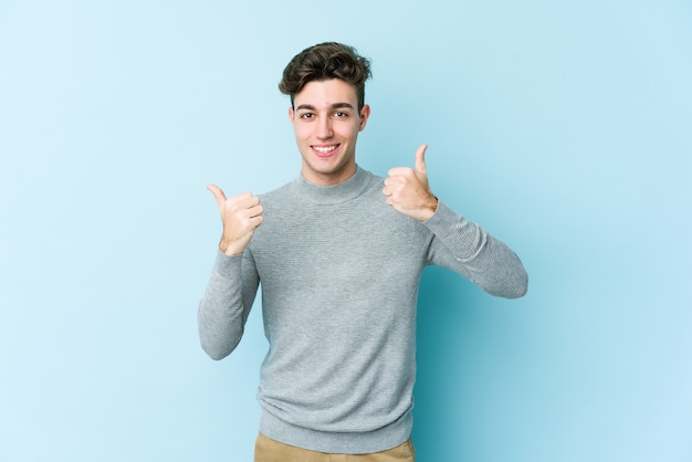 Hombre caucásico joven aislado en la pared azul levantando ambos pulgares, sonriente y confiado.