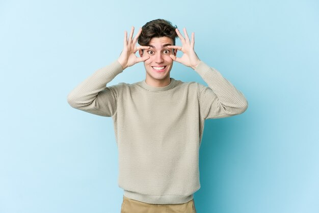 Hombre caucásico joven aislado en la pared azul manteniendo los ojos abiertos para encontrar una oportunidad de éxito.