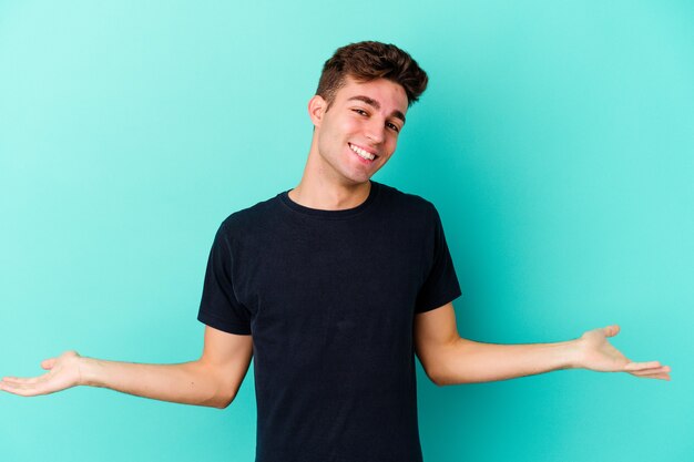 Hombre caucásico joven aislado en la pared azul que muestra una expresión de bienvenida.