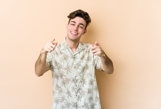 Hombre caucásico joven aislado en la pared beige apuntando al frente con los dedos.