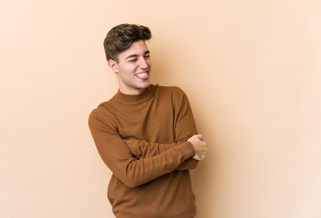 Hombre caucásico joven aislado en la pared beige divertido y amistoso sacando la lengua.