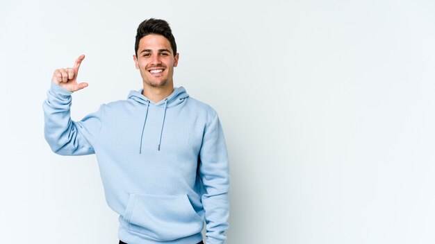 Foto hombre caucásico joven aislado en la pared blanca sosteniendo algo pequeño con los dedos índices, sonriente y confiado.