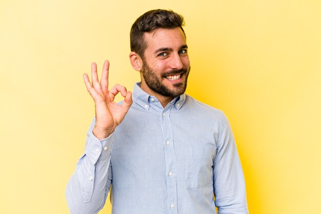 Foto hombre caucásico joven aislado sobre fondo amarillo alegre y confiado mostrando gesto ok