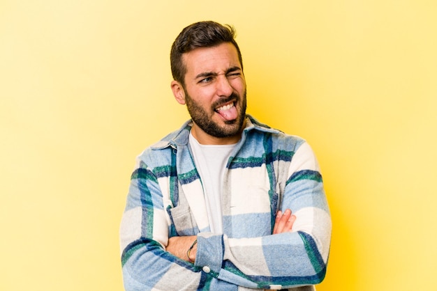 Hombre caucásico joven aislado sobre fondo amarillo divertido y amigable sacando la lengua