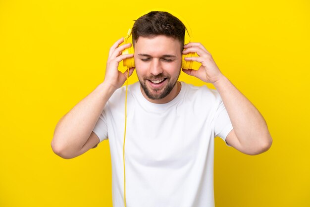 Hombre caucásico joven aislado sobre fondo amarillo escuchando música