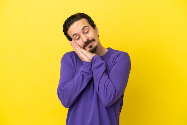 Hombre caucásico joven aislado sobre fondo amarillo haciendo gesto de sueño en expresión adorable