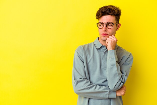 Hombre caucásico joven aislado sobre fondo amarillo mirando hacia los lados con expresión dudosa y escéptica.