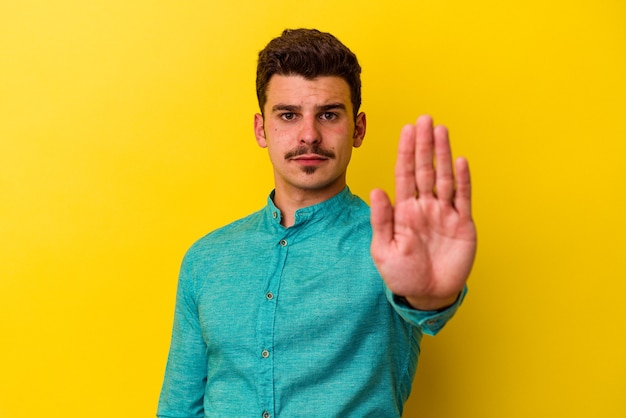 Hombre caucásico joven aislado sobre fondo amarillo de pie con la mano extendida mostrando la señal de stop, impidiéndote.