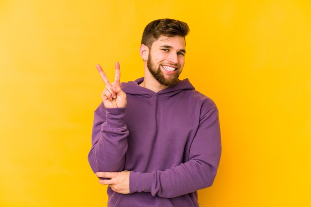 Hombre caucásico joven aislado sobre fondo amarillo que muestra el número dos con los dedos.