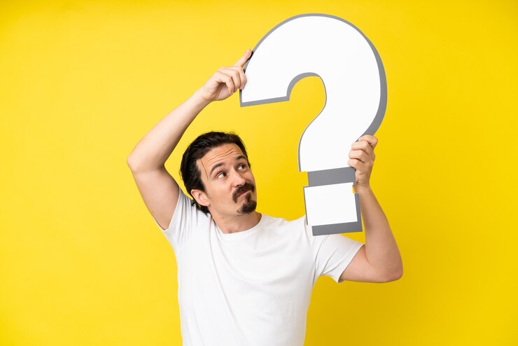 Foto hombre caucásico joven aislado sobre fondo amarillo sosteniendo un icono de signo de interrogación
