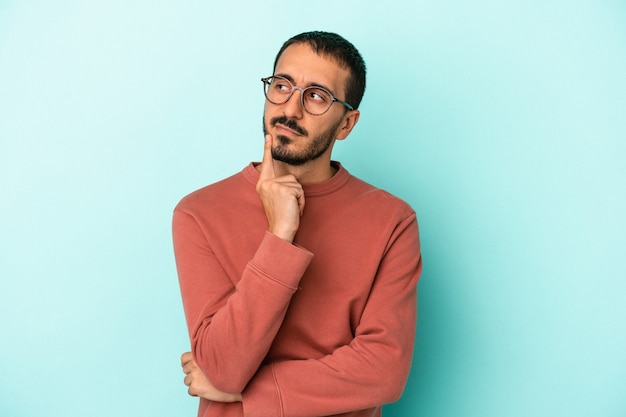 Hombre caucásico joven aislado sobre fondo azul contemplando, planificando una estrategia, pensando en la forma de un negocio.