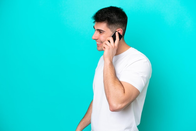 Hombre caucásico joven aislado sobre fondo azul manteniendo una conversación con el teléfono móvil con alguien