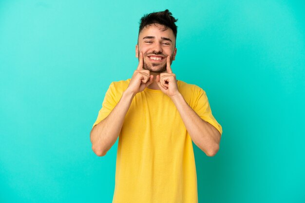 Hombre caucásico joven aislado sobre fondo azul sonriendo con una expresión feliz y agradable