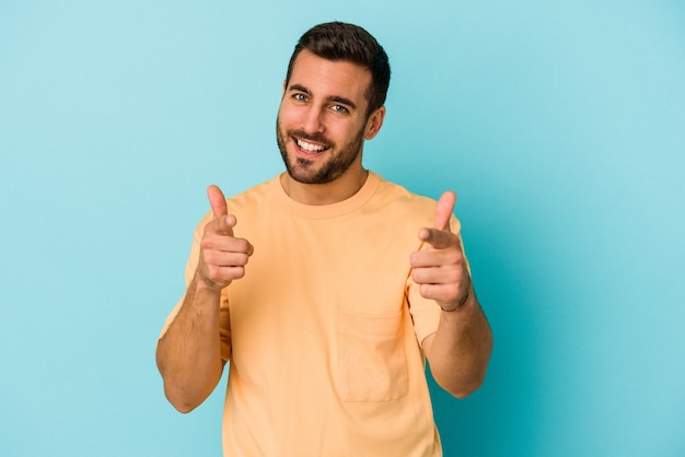 Hombre caucásico joven aislado sobre fondo azul sonrisas alegres apuntando al frente.