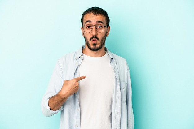 Hombre caucásico joven aislado sobre fondo azul sorprendido señalando con el dedo, sonriendo ampliamente.