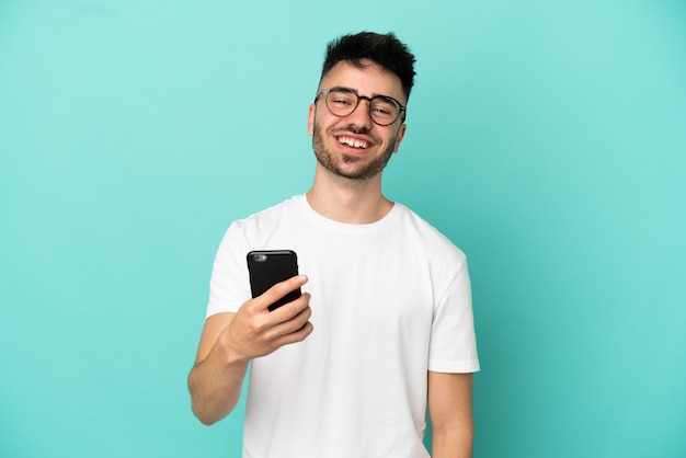 Hombre caucásico joven aislado sobre fondo azul mediante teléfono móvil