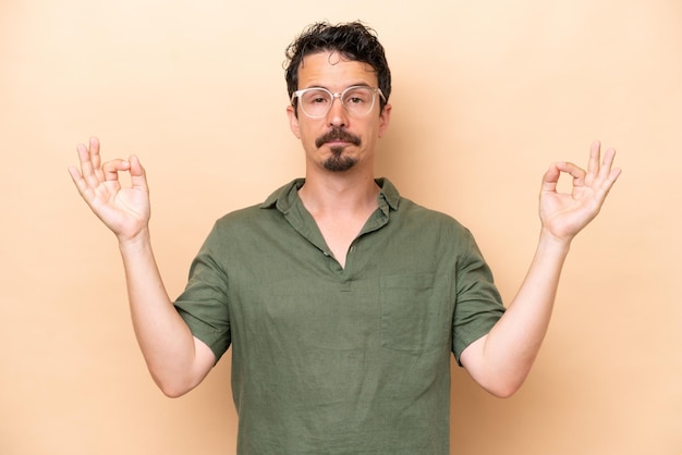 Hombre caucásico joven aislado sobre fondo beige en pose zen