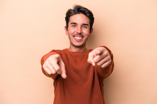 Hombre caucásico joven aislado sobre fondo beige sonrisas alegres apuntando al frente.