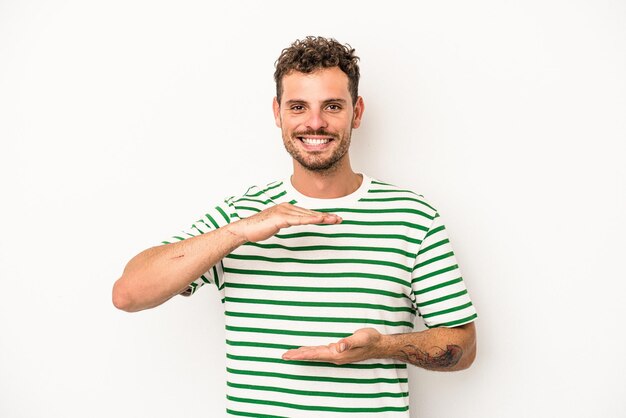 Foto hombre caucásico joven aislado sobre fondo blanco sosteniendo algo con ambas manos, presentación del producto.