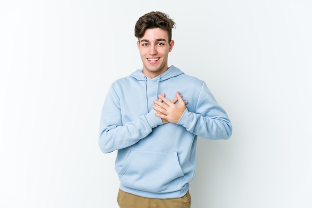 Hombre caucásico joven aislado sobre fondo blanco tiene expresión amistosa, presionando la palma contra el pecho. Concepto de amor.