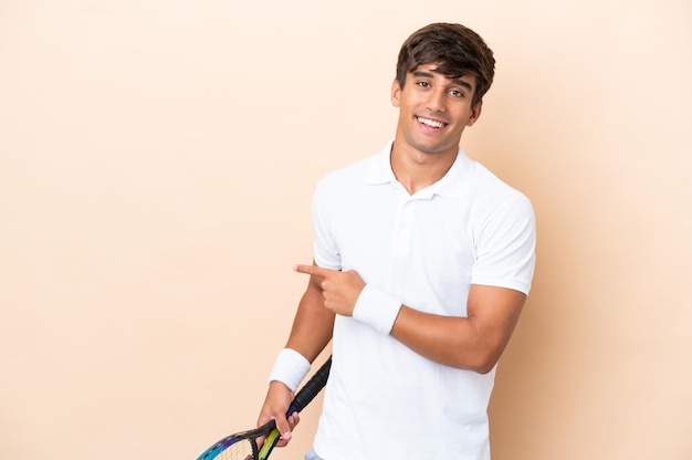 Hombre caucásico joven aislado sobre fondo ocre jugando tenis y apuntando hacia el lateral