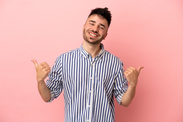 Hombre caucásico joven aislado sobre fondo rosa con gesto de pulgar hacia arriba y sonriendo