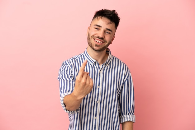 Hombre caucásico joven aislado sobre fondo rosa haciendo gesto que viene