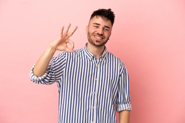 Hombre caucásico joven aislado sobre fondo rosa mostrando signo ok con los dedos