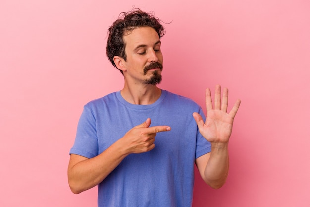 Hombre caucásico joven aislado sobre fondo rosa sonriendo alegre mostrando el número cinco con los dedos.