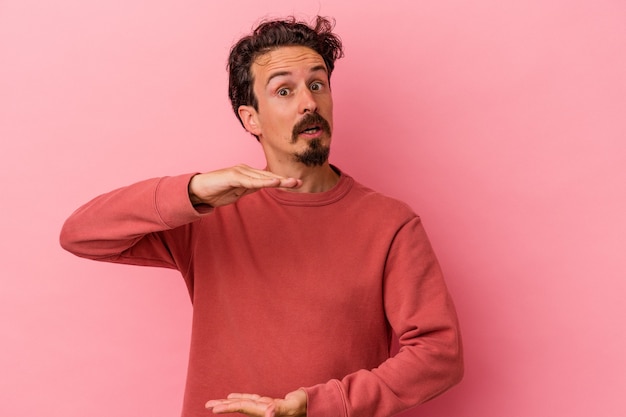 Hombre caucásico joven aislado sobre fondo rosa sosteniendo algo con ambas manos, presentación del producto.