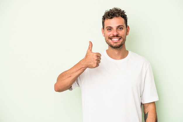 Hombre caucásico joven aislado sobre fondo verde sonriendo y levantando el pulgar